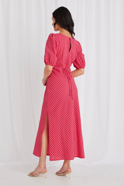 model wears a long gingham pink dress and heels