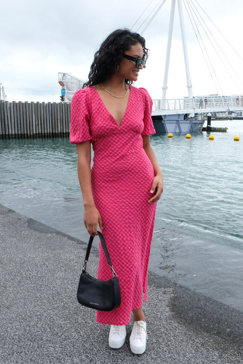 model wears a long gingham pink dress and heels with black handbag and white sneakers