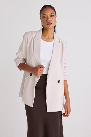 Model wears a bone blazer with a white singlet and skirt. 