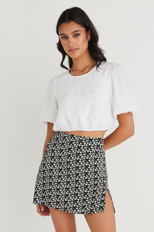 Model wears a white top with a black and white skirt. 