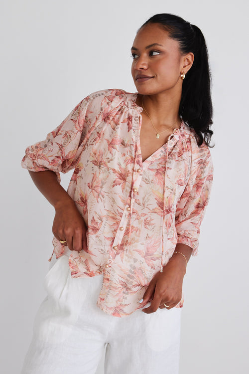 Model wears a floral blouse with white linen pants.