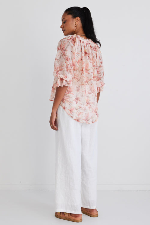 Model wears a floral blouse with white linen pants.