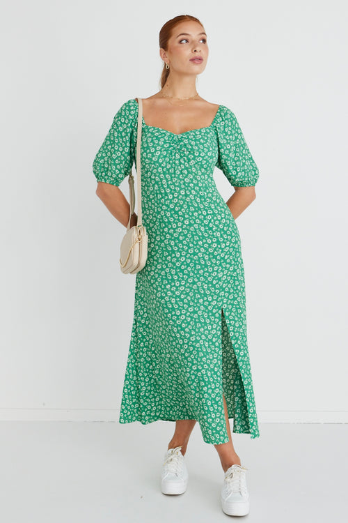 Model wears a green floral print maxi dress with white sneakers and a beige handbag.  