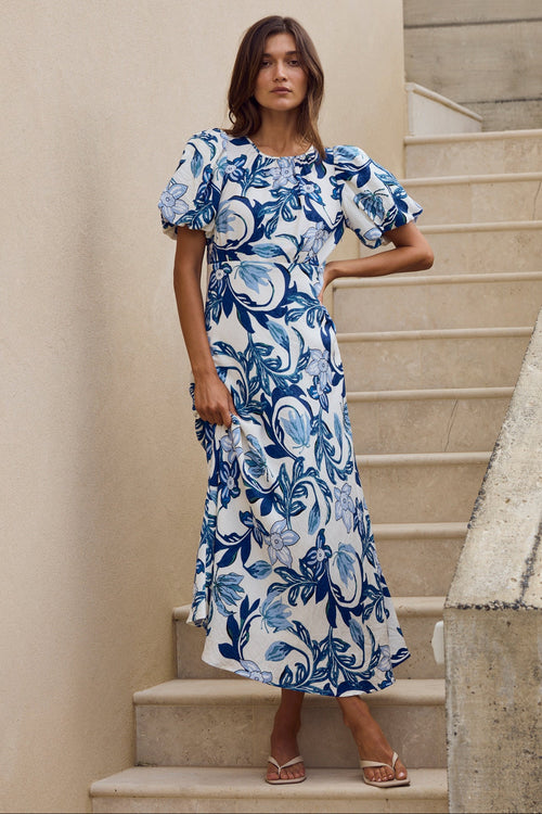 Woman in a blue floral dress standing on stone steps outdoors