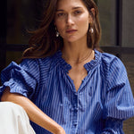 Woman wearing a blue shirt and white pants sitting on steps.