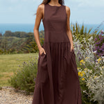 Woman in a brown dress standing outdoors with greenery and flowers in the background
