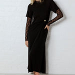 Woman wearing a black dress with lace sleeves against a white wall