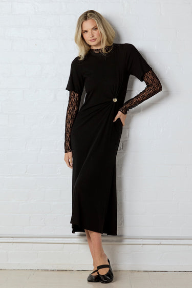 Woman wearing a black dress with lace sleeves against a white wall
