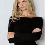 Woman wearing a black top and blue jeans against a white brick wall
