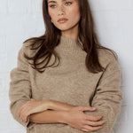 Woman wearing a beige sweater against a white brick wall