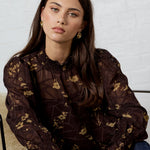 Woman sitting on a chair wearing a dark floral blouse and jeans against a light background