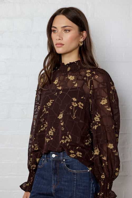 Woman wearing a dark floral blouse against a white brick wall