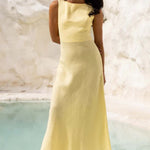 Woman in a yellow dress standing against a white marble wall.