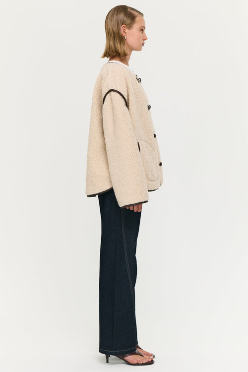 Person wearing a beige jacket with black accents on a white background