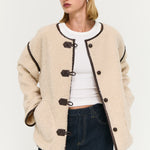 Woman wearing a beige duffle coat with black buttons on a white background