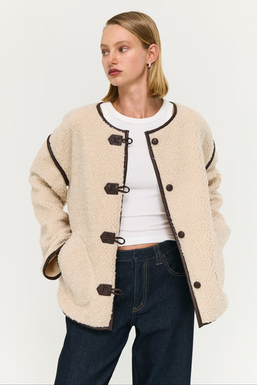 Woman wearing a beige duffle coat with black buttons on a white background