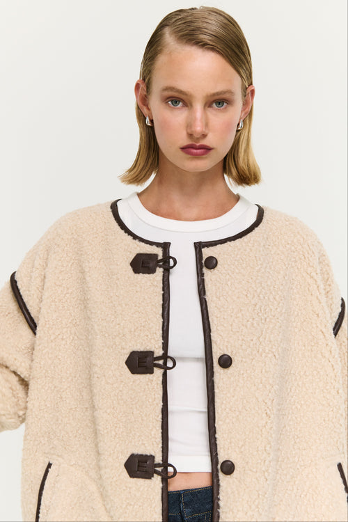 Woman wearing a beige coat with black buttons on a white background