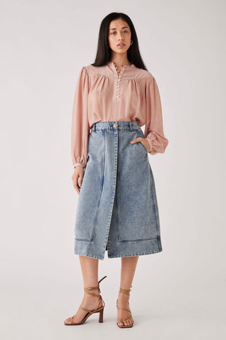 Model wears a pink blouse with a denim skirt