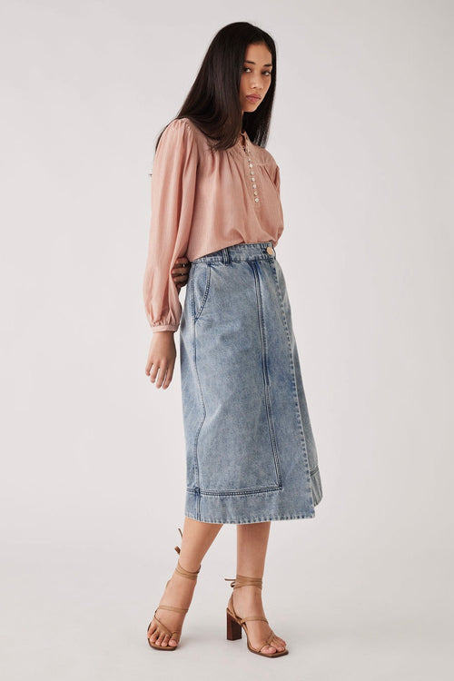 Model wears a pink blouse with a denim skirt