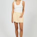 Woman wearing a white tank top and beige skirt on a plain background