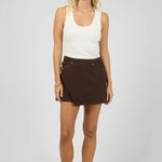 Woman wearing a white tank top and brown skirt on a plain background