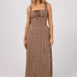 A woman modeling a brown and beige gingham maxi dress with a tie-front bodice, photographed against a plain light gray studio background.
