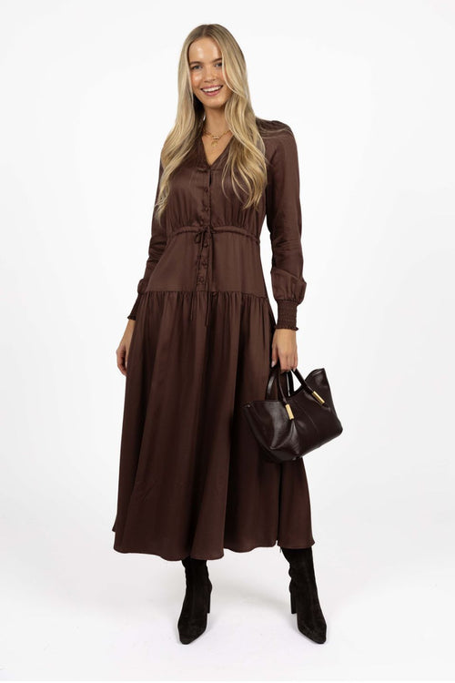 Woman wearing a brown dress holding a matching handbag on a white background