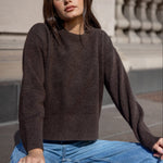 Woman wearing a brown sweater and blue jeans sitting on steps.