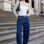 Woman in white top and blue jeans standing on stone steps in front of a classical building.