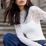 Woman wearing a white lace top and blue jeans sitting on steps.