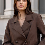 Woman wearing a brown coat with a blurred architectural background