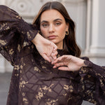 Woman wearing a dark floral lace dress with a blurred architectural background