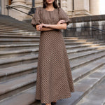 Woman in a patterned dress standing on stone steps in front of a classical building.