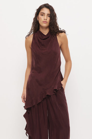 A woman modeling a sleeveless, dark burgundy draped top and matching wide-leg pants set, paired with black flip-flops, against a plain white studio background.