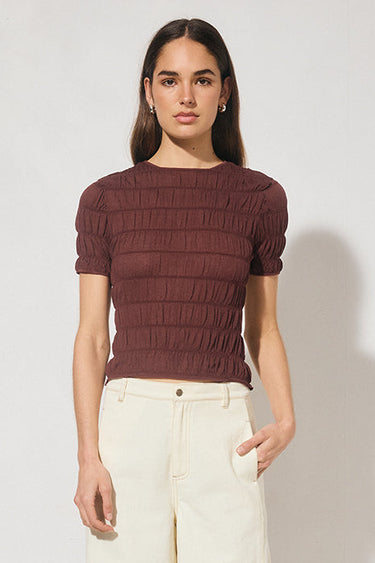 Woman wearing a brown ribbed sweater and beige pants on a white background