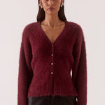 Woman wearing a burgundy cardigan and dark pants on a white background