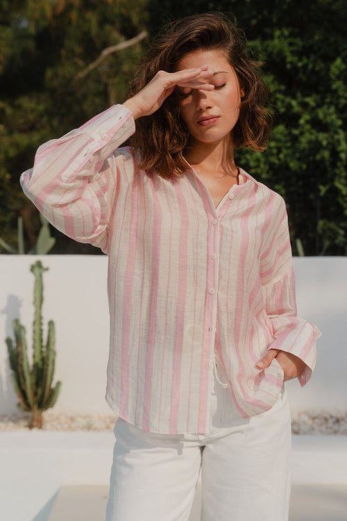 Woman wearing a pink and white striped shirt with a blurred outdoor background