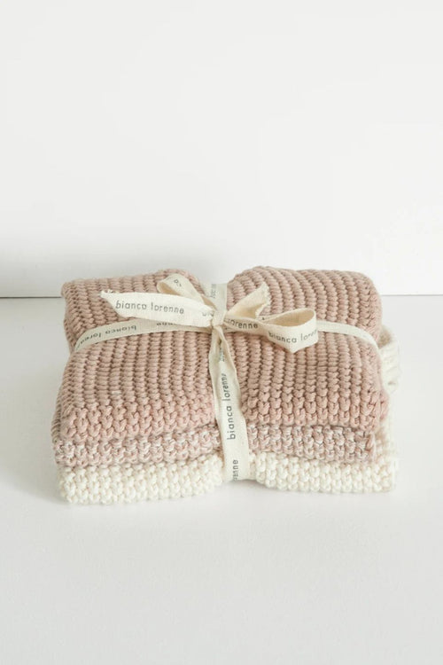 Two folded chunky-knit baby blankets in dusty pink and cream, tied together with a cream ribbon printed with the brand name 'bianco foraggio'.