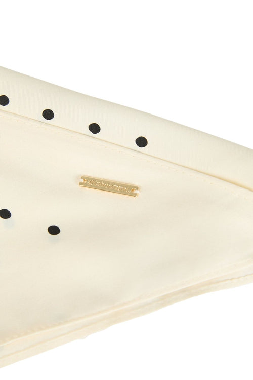 Close-up of a cream-colored leather clutch or wallet featuring black circular studs and a small gold-tone metal brand plaque.