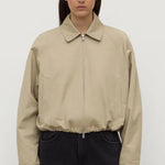 Person wearing a beige jacket and black pants on a white background