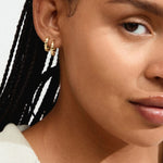 Close-up of a woman's ear with gold earrings against a neutral background