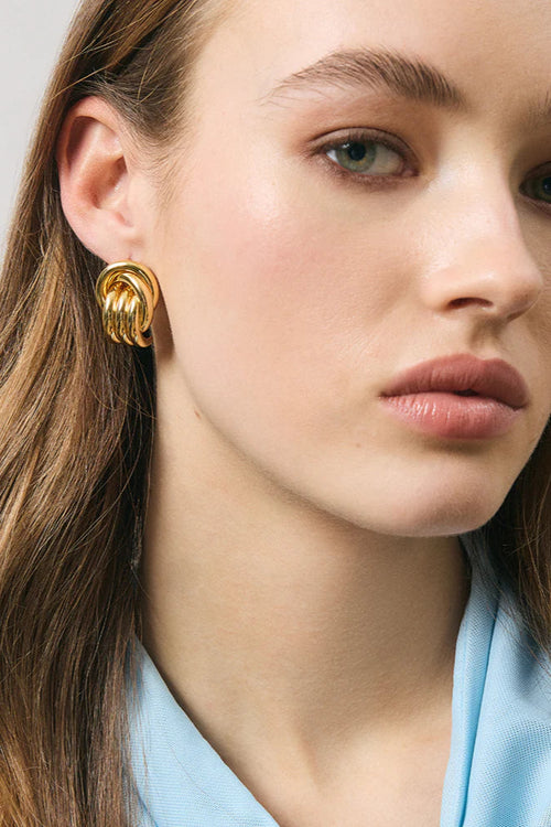 Close-up of a woman wearing gold earrings with a neutral background