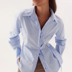 Woman wearing a light blue button-up shirt with a belt, standing against a white background
