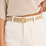 Person wearing a beige sweater and white pants with a beige belt.
