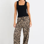 Woman wearing a black sleeveless top and leopard print pants on a white background