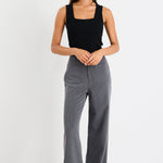 Woman wearing a black sleeveless top and gray flared pants on a white background