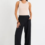 Woman wearing a beige sleeveless top and black wide-leg pants on a white background