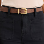 Person wearing black pants with a brown belt and beige top on a white background