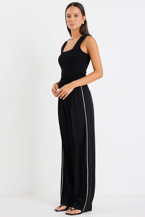 Woman wearing a black sleeveless top and wide-leg pants with a white stripe on a white background