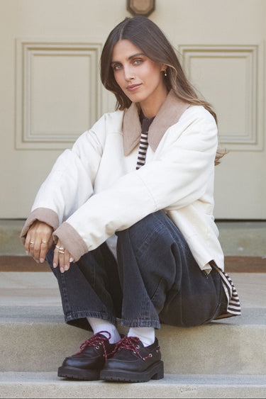 Woman sitting on steps wearing a white coat and dark jeans.